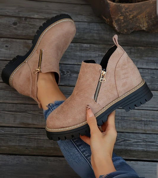 Beige ankle boots with zippers held by a hand on a wooden floor.