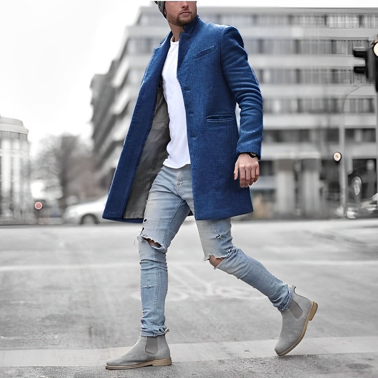 Man wearing a blue coat, white shirt, ripped jeans, and gray boots on a city street.