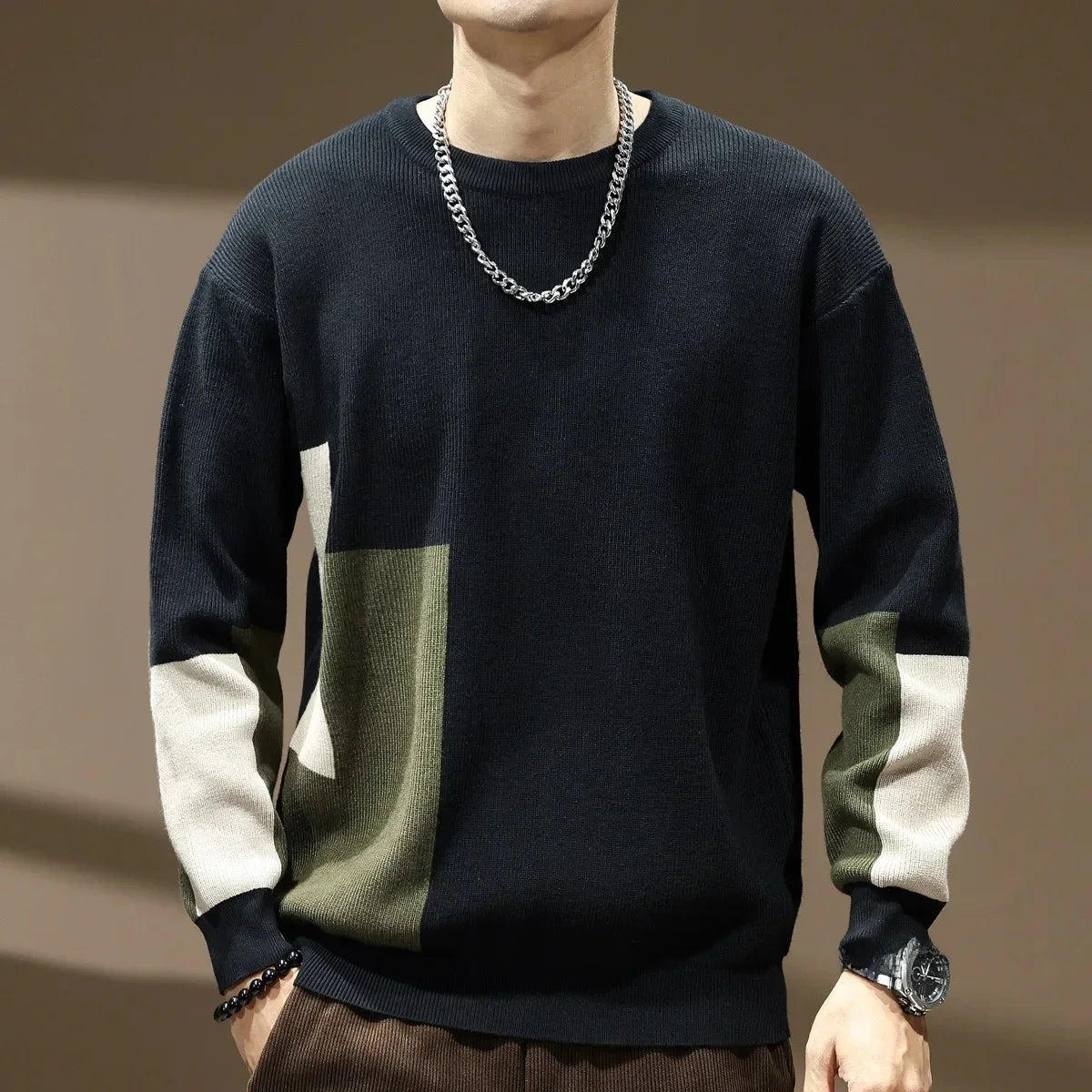 Person wearing a black, green, and beige sweater with a chain necklace on a brown background