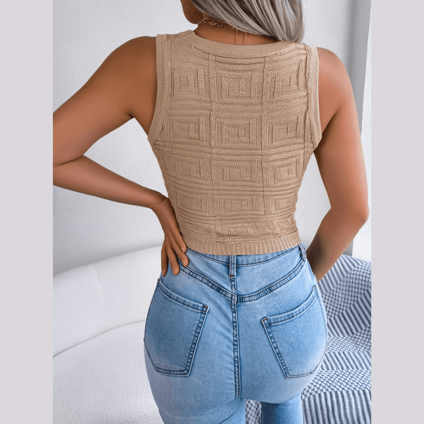 Person wearing a beige textured tank top and blue jeans with a neutral background