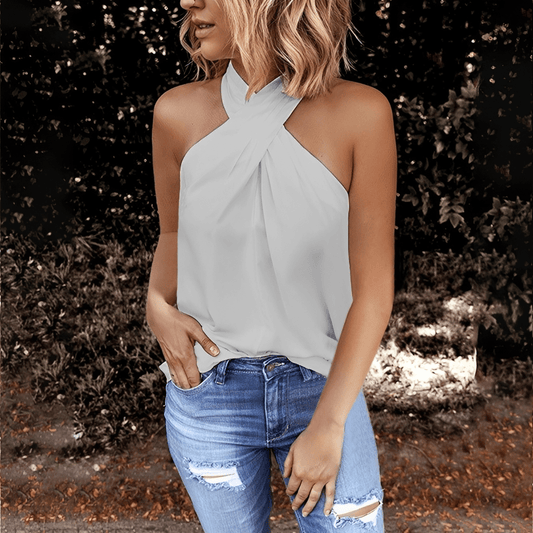 Woman wearing a light gray halter top and blue jeans outdoors.