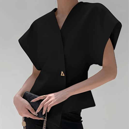 Black sleeveless top with a gold triangle detail held by a person against a gray background