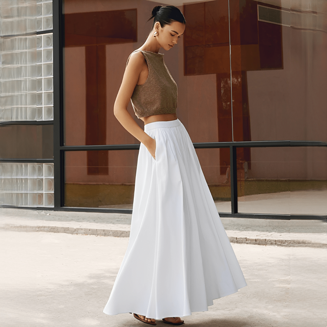 Woman in a brown top and white skirt standing in front of a modern building.
