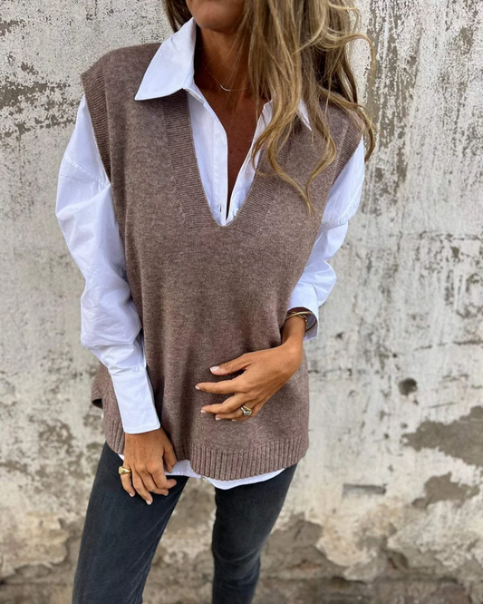 Person wearing a brown sweater vest over a white shirt with a neutral background