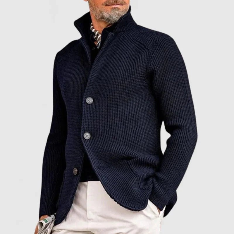 Man wearing a navy blue knitted cardigan over a patterned shirt on a light gray background