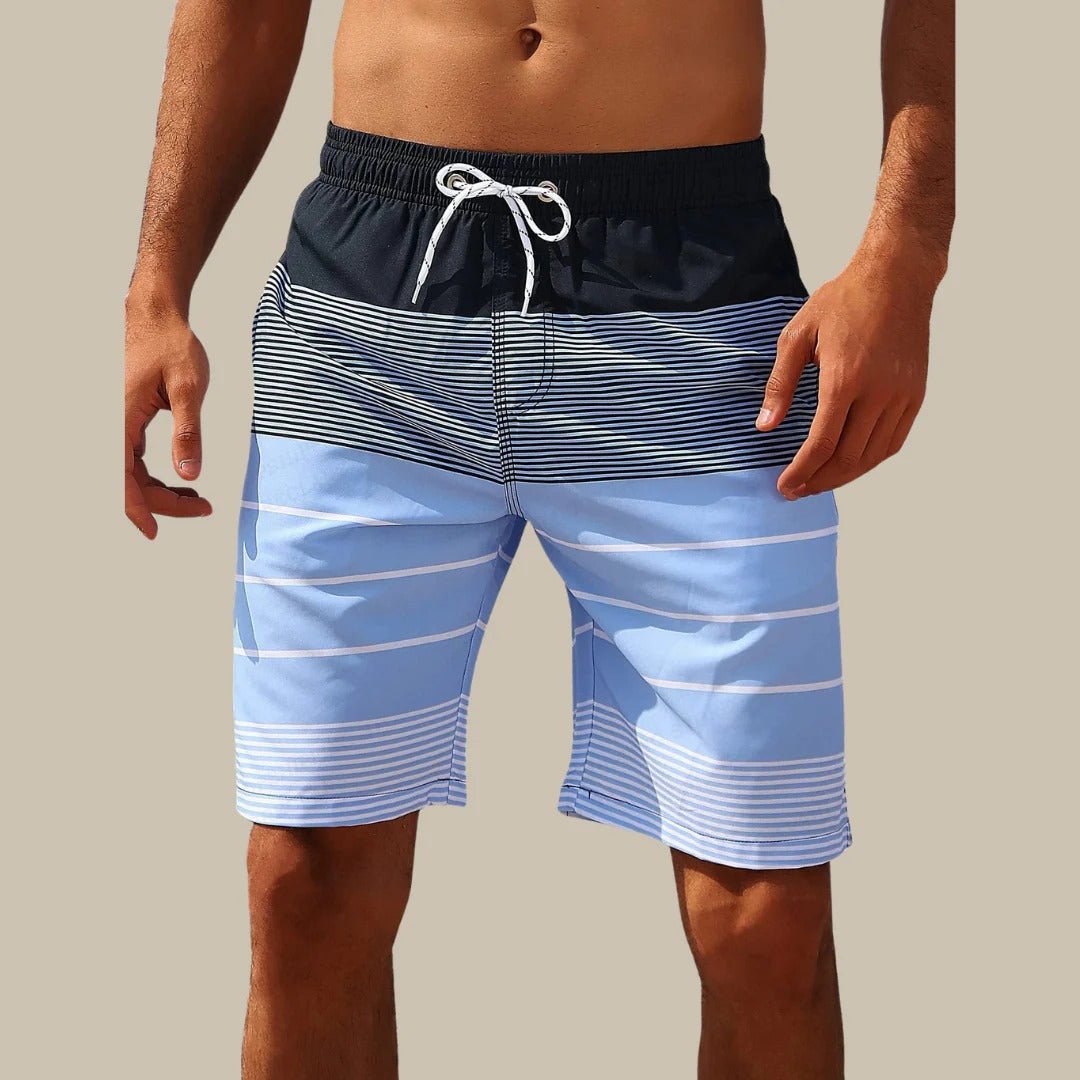 Blue and black striped swim shorts with a white drawstring on a beige background