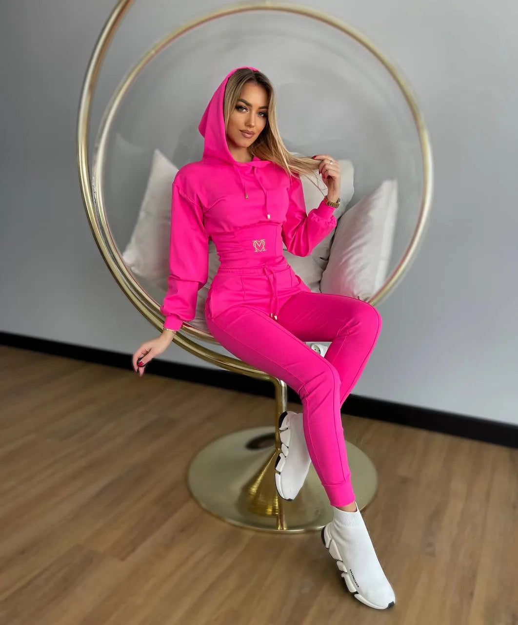 Woman in a bright pink tracksuit sitting on a modern chair.
