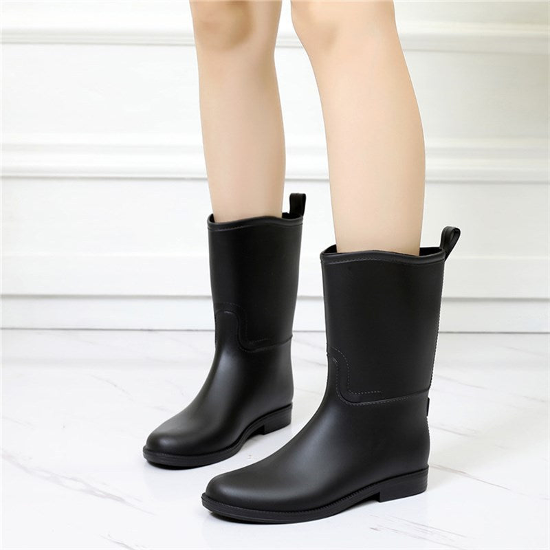 Black rain boots worn with light-colored pants on a white background