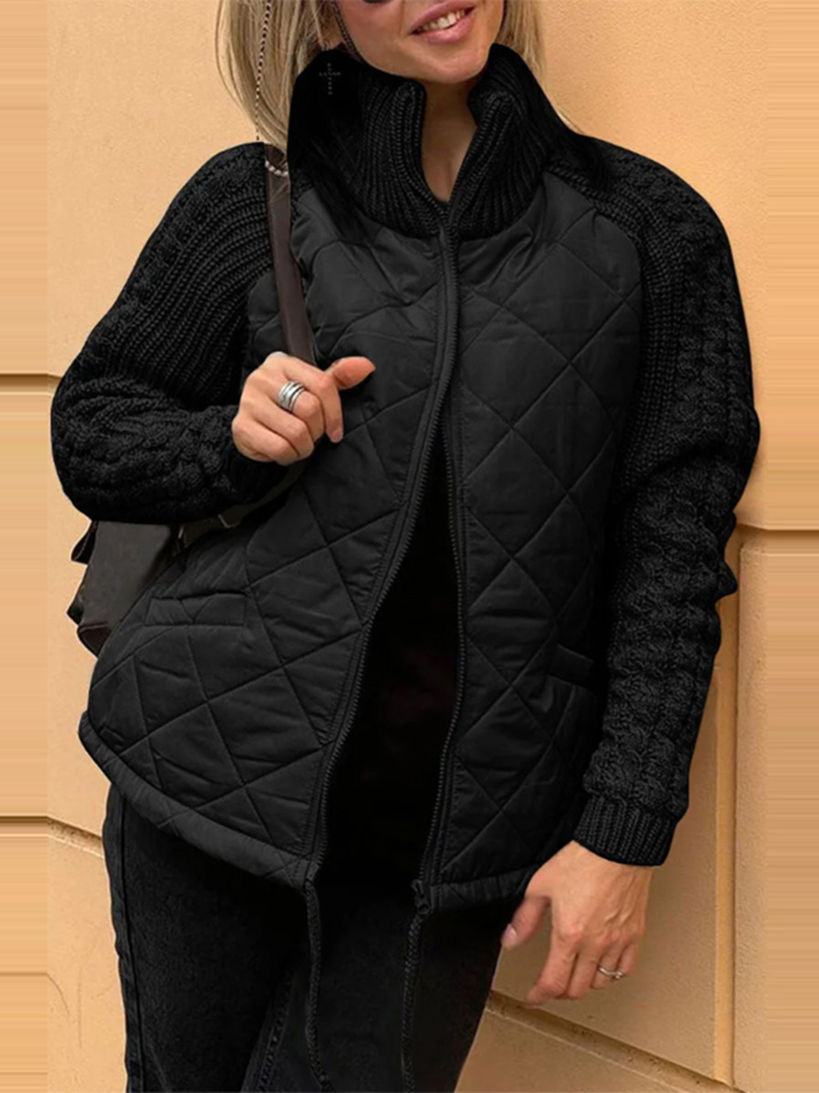 Person wearing a black quilted vest over a black sweater against a beige wall.