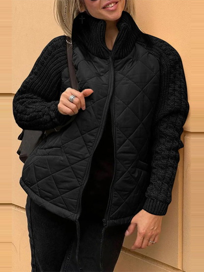 Person wearing a black quilted vest over a black sweater against a beige wall.