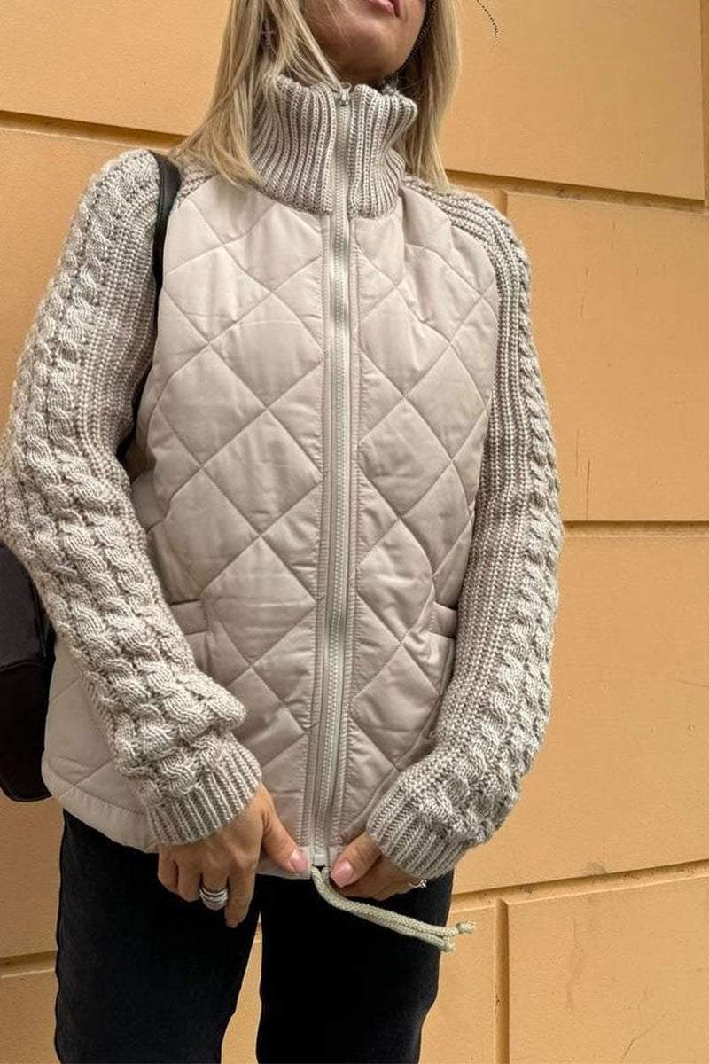 Person wearing a quilted beige vest over a knitted sweater against a beige wall.