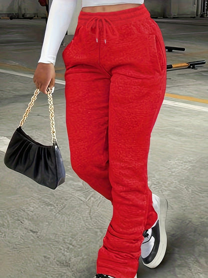 Person wearing red sweatpants holding a black handbag on a concrete floor.