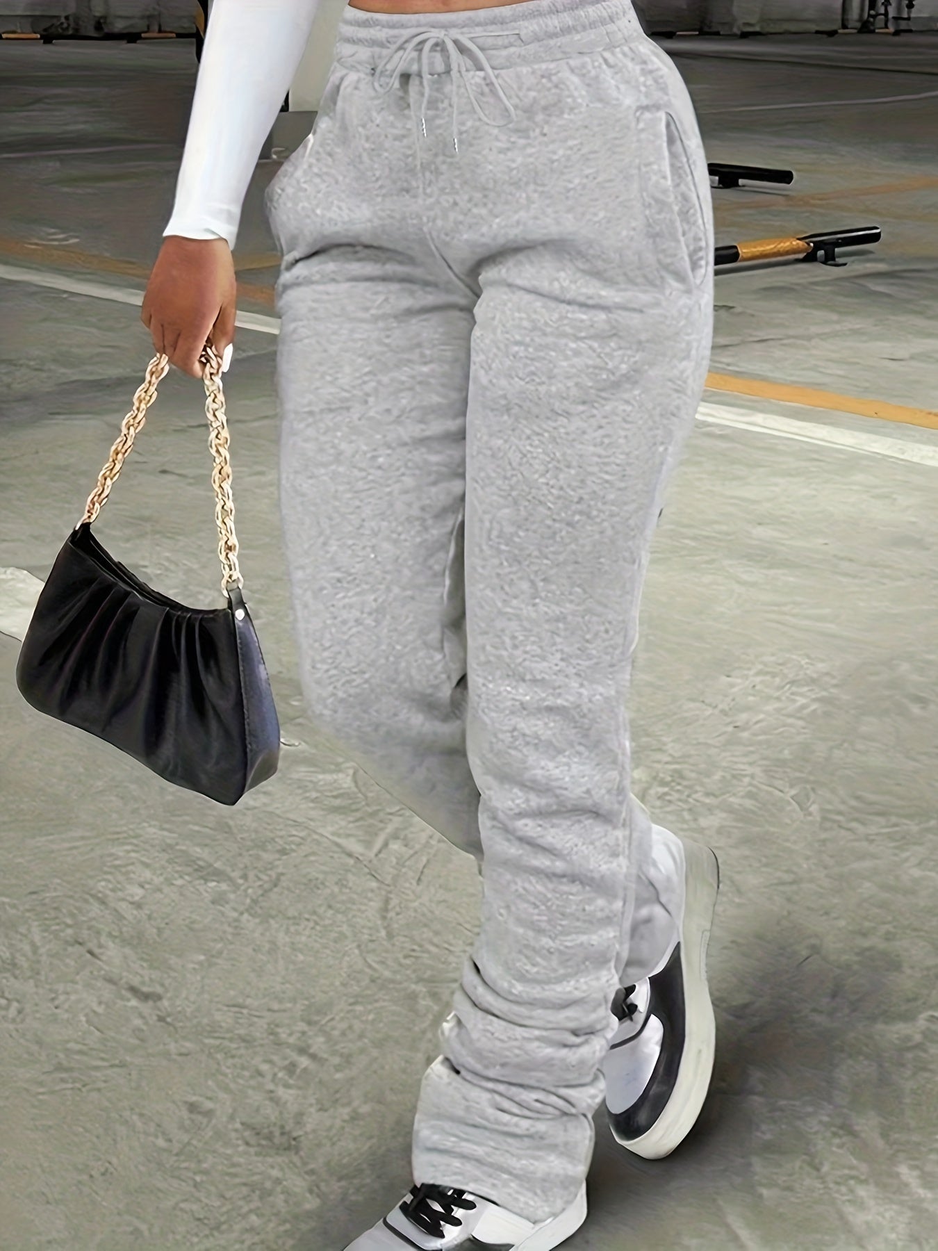 Person wearing gray sweatpants holding a black handbag on a concrete surface