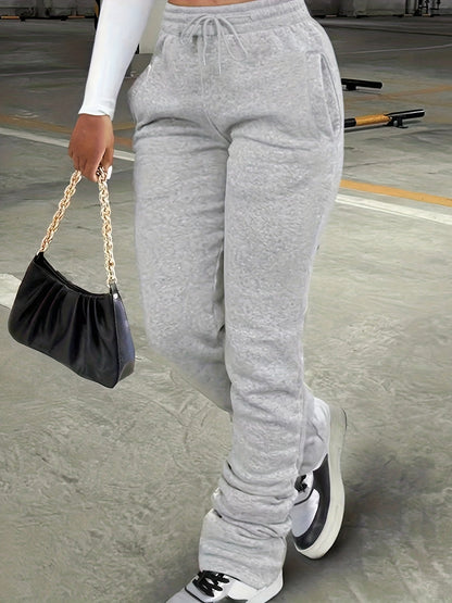 Person wearing gray sweatpants holding a black handbag on a concrete surface