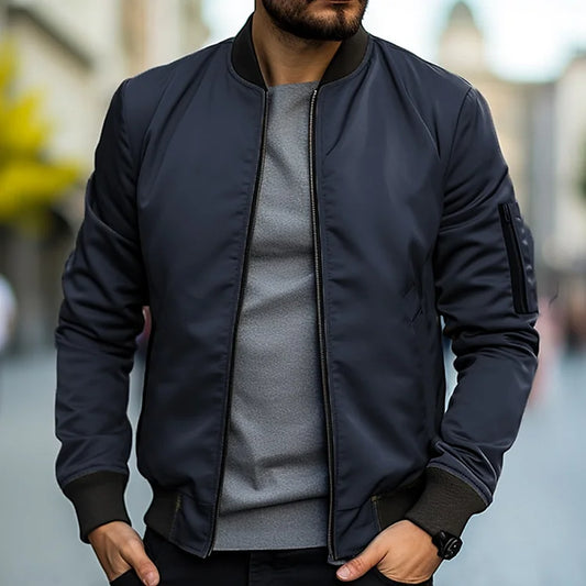 Man wearing a dark blue bomber jacket over a gray shirt with a blurred background