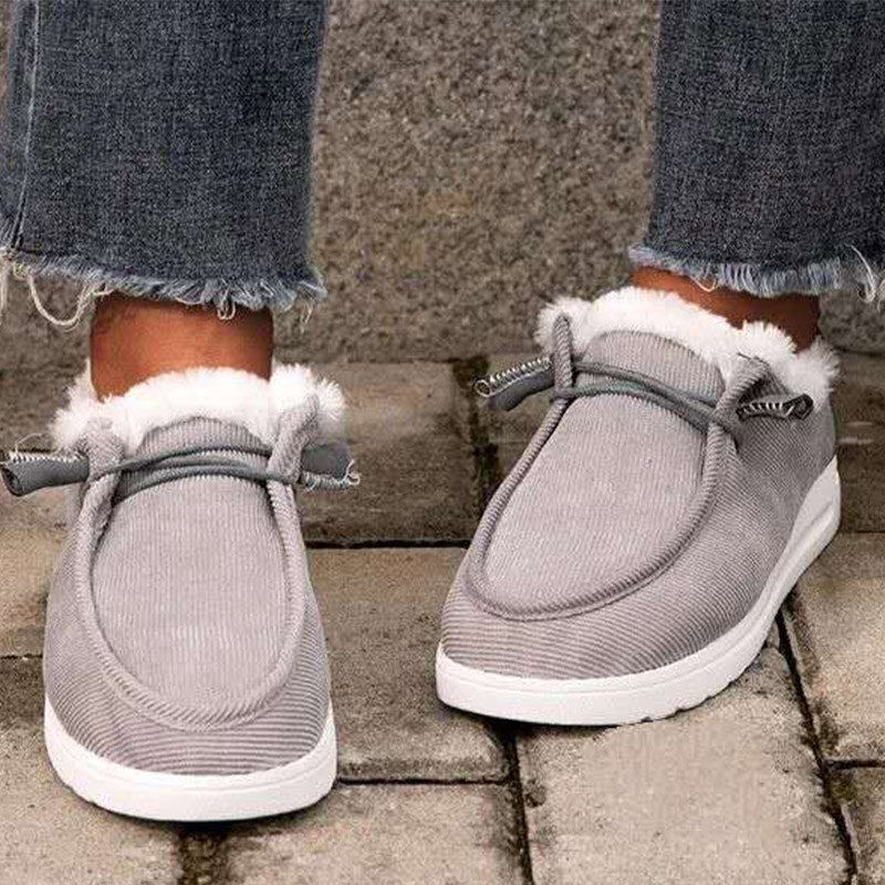 Gray slippers with white fur trim worn by a person on a stone pavement.