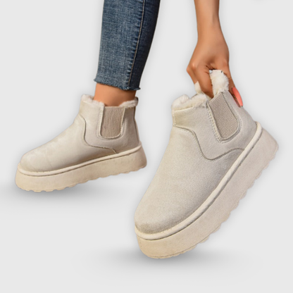 Beige ankle boots with white soles worn by a person on a light gray background