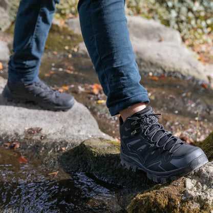 Person wearing black hiking boots stepping onto a rock with a natural background