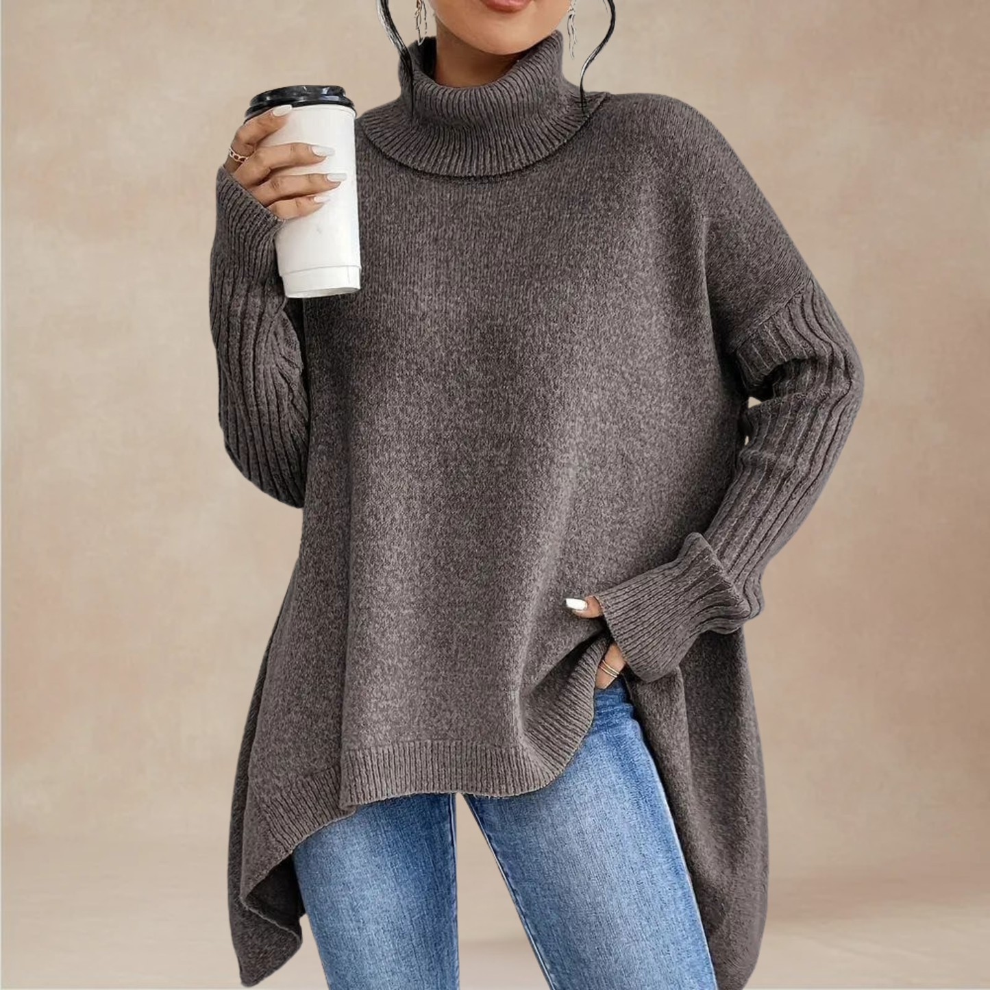 Person wearing a gray turtleneck sweater and blue jeans, holding a white cup.