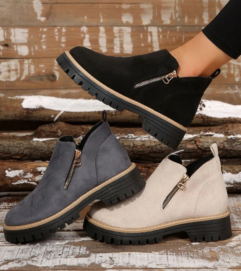 Black, gray, and beige ankle boots with zippers on a wooden background