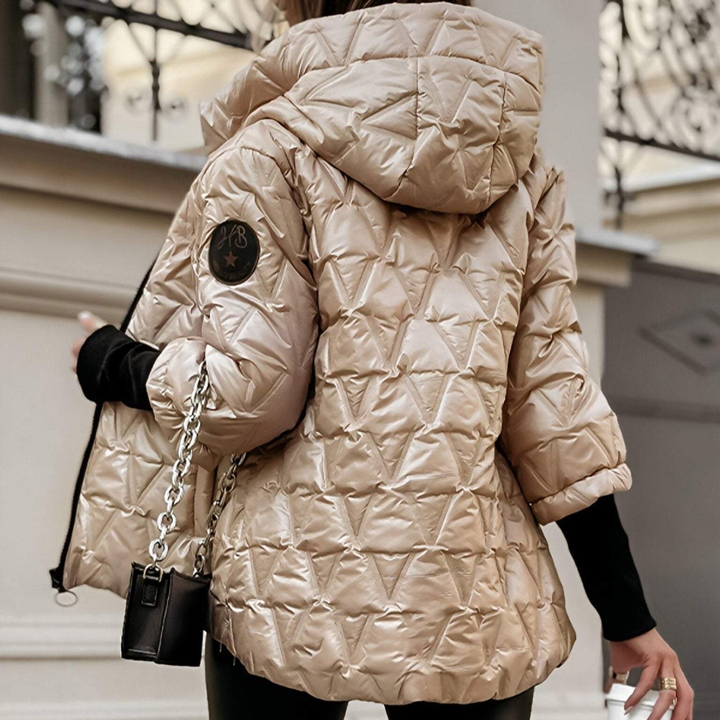 Person wearing a beige quilted jacket with a brand logo, holding a black handbag.