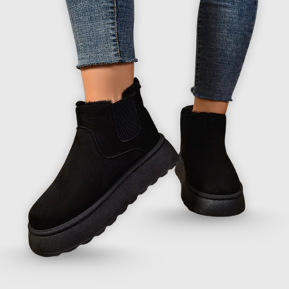 Black ankle boots worn with blue jeans on a light gray background