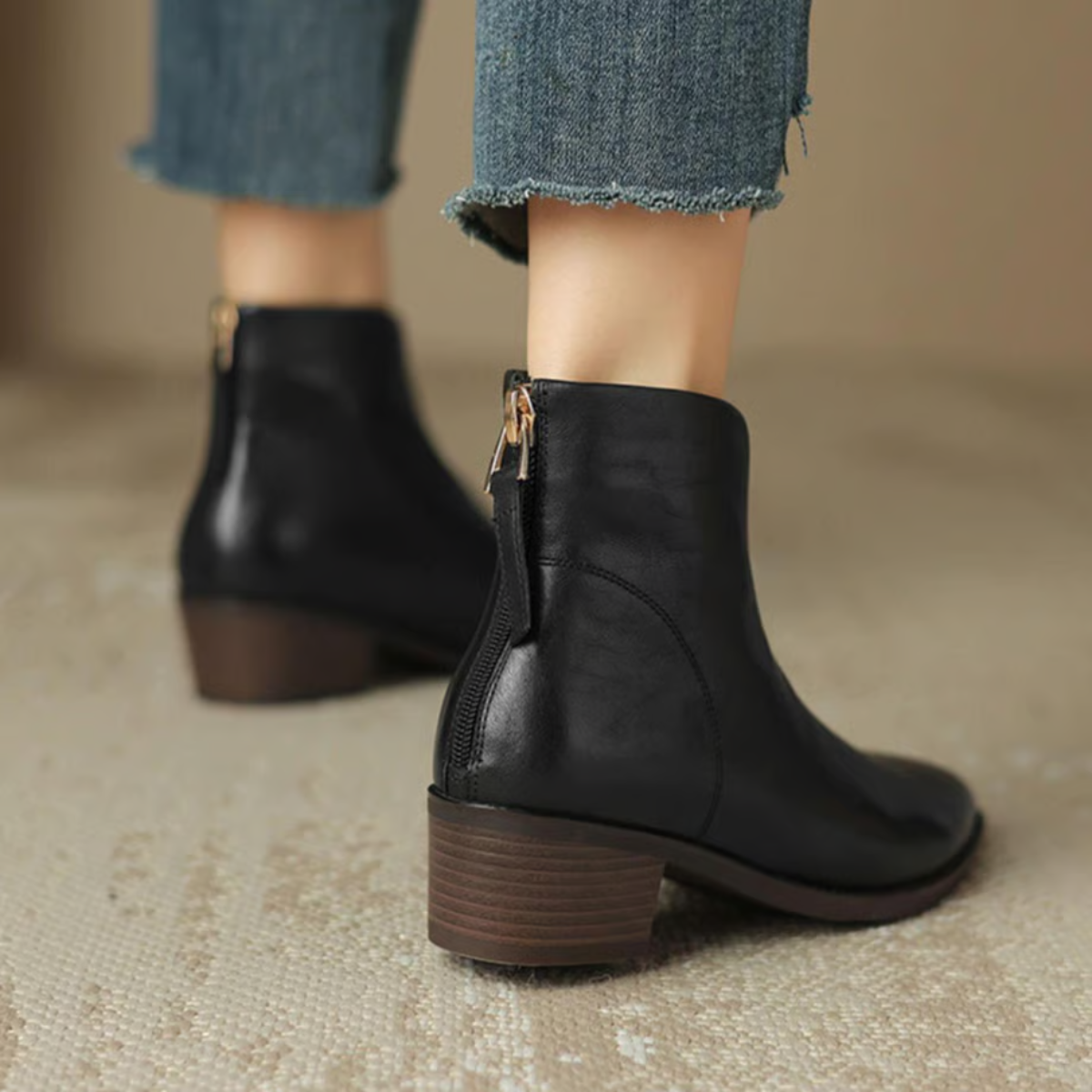 Black ankle boots worn with jeans on a neutral background