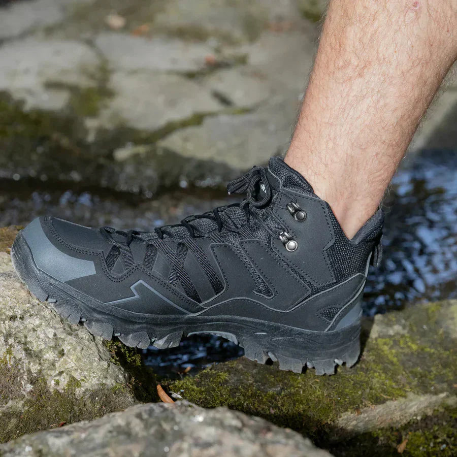 Black hiking boot on a rocky surface with water in the background