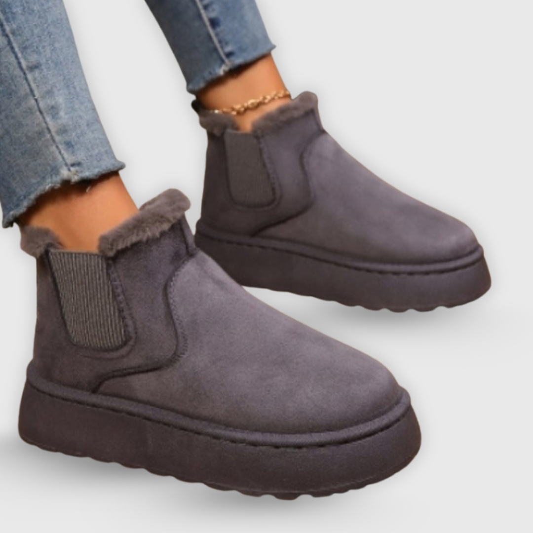 Gray ankle boots with fur trim worn with blue jeans on a light gray background
