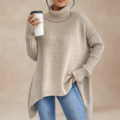 Person wearing a beige turtleneck sweater and blue jeans, holding a white cup with a black lid.