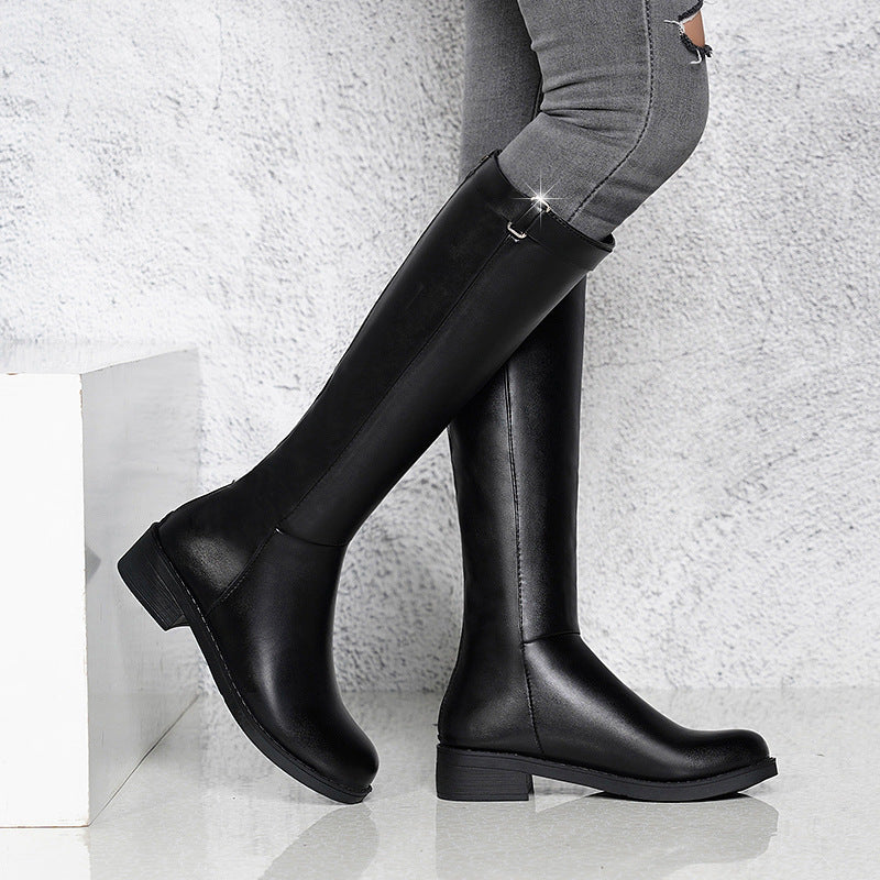 Black knee-high boots worn with gray pants on a light background