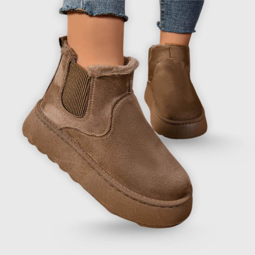Brown suede ankle boots worn with rolled-up jeans on a light gray background