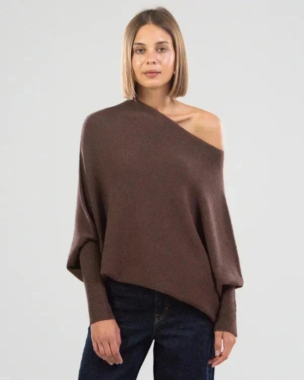 Woman wearing a brown one-shoulder sweater against a plain background