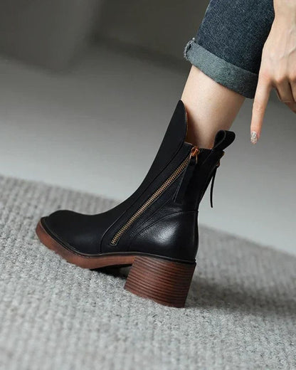 Black ankle boot with brown sole worn by a person on a neutral background