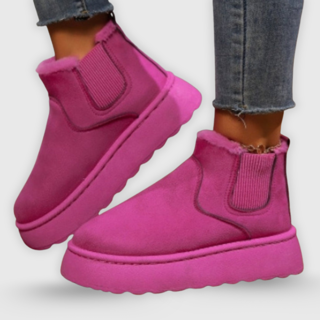 Pink slip-on boots worn with jeans on a light gray background