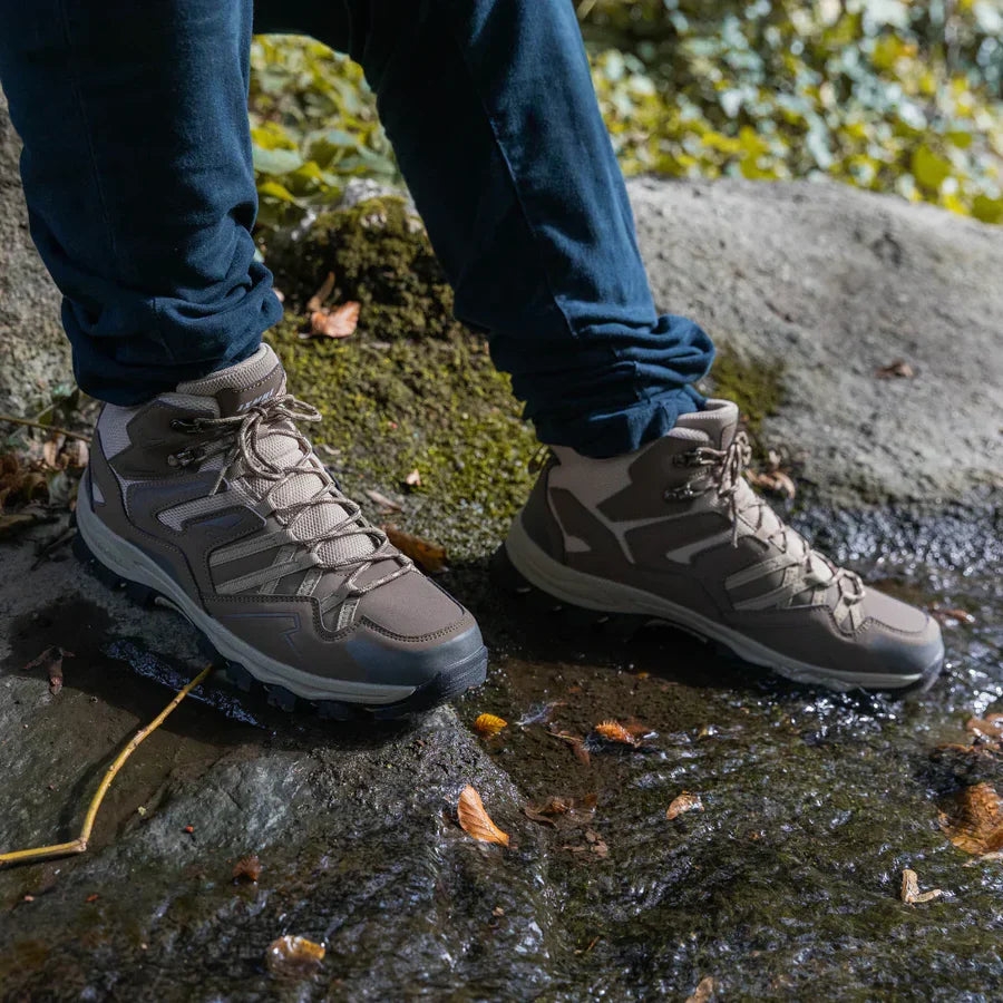 Person wearing gray hiking boots on a rocky surface with greenery.