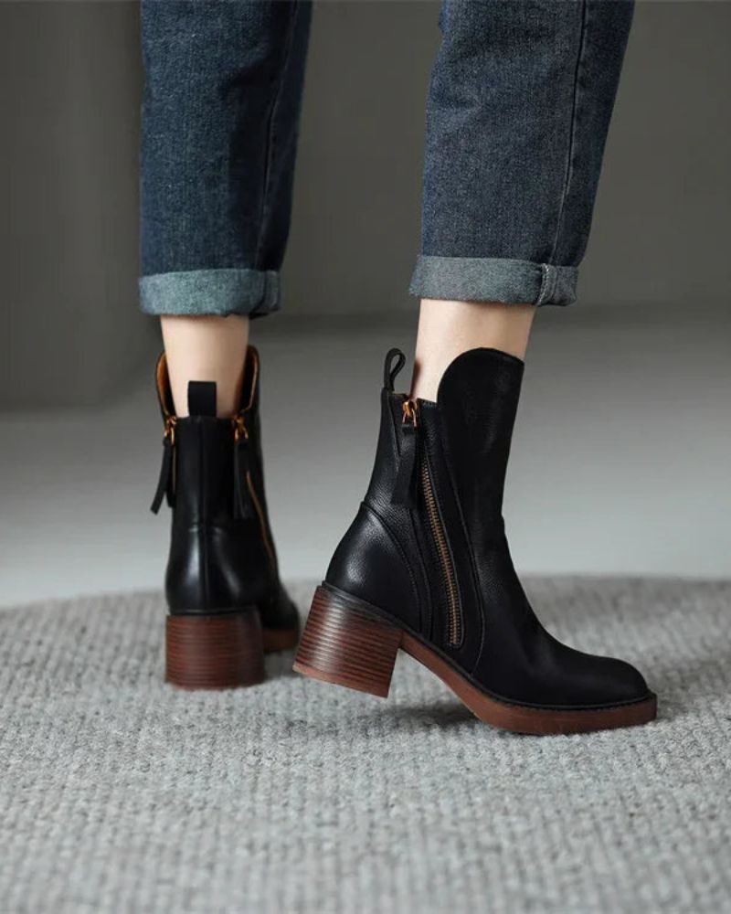 Black leather boots with brown soles worn with rolled-up jeans on a neutral background
