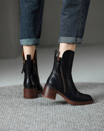 Black leather boots with brown soles worn with rolled-up jeans on a neutral background