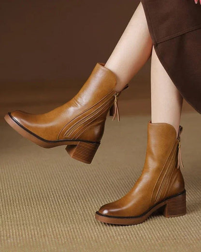 Brown leather ankle boots worn by a person on a brown textured background