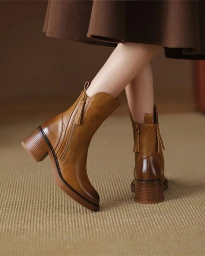 Brown leather boots worn with a brown skirt on a neutral background