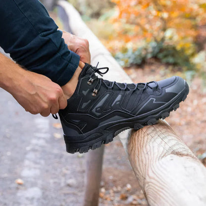 Person tying a black hiking boot outdoors with a blurred natural background