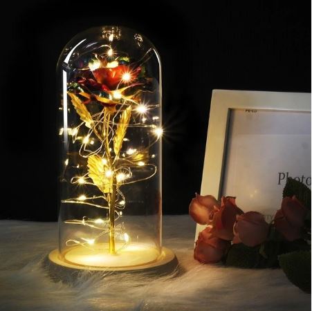 Gold rose inside a glass dome with LED lights on a dark background