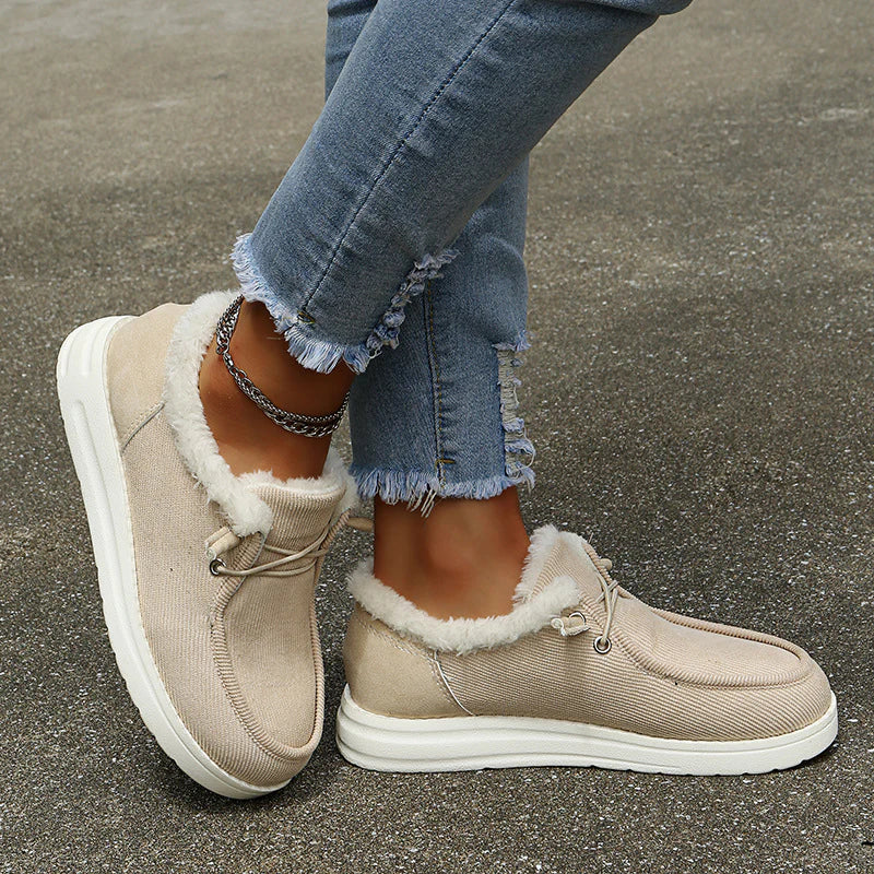 Beige sneakers with white fur lining worn with blue jeans on a concrete surface