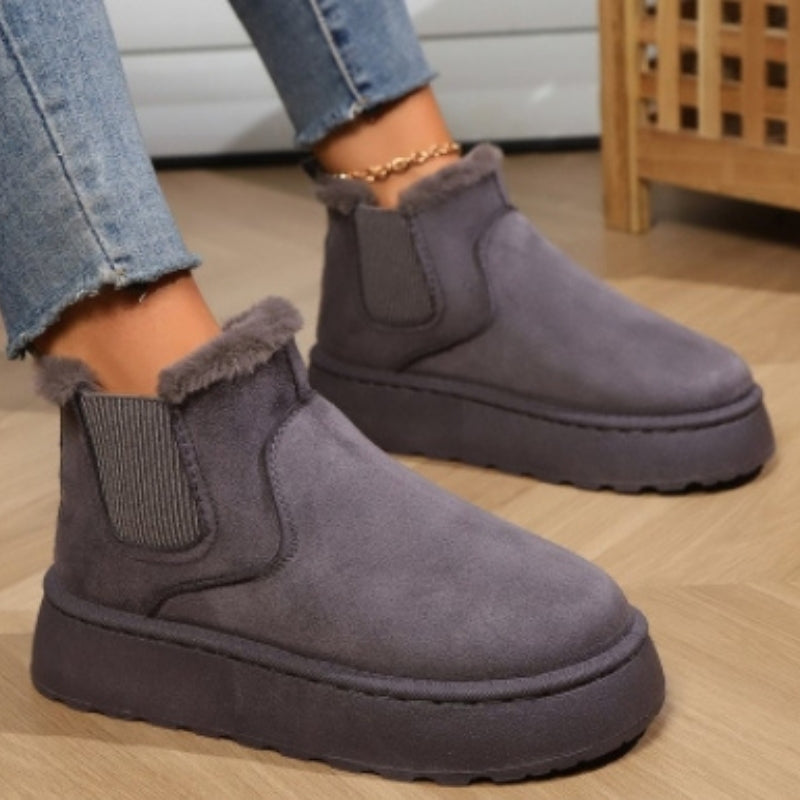 Gray suede ankle boots with fur trim worn indoors on a wooden floor.