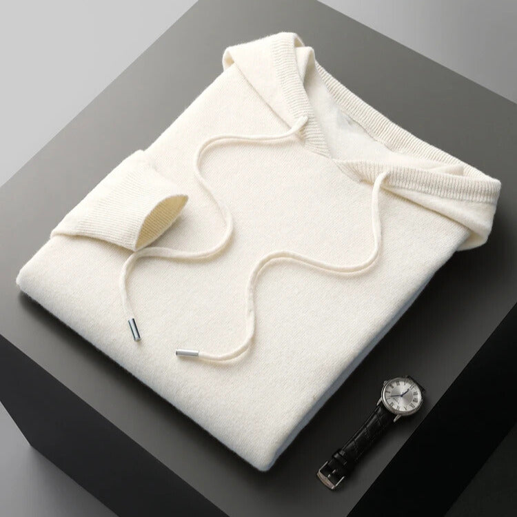 Folded white hoodie on a dark surface with a watch and pen nearby