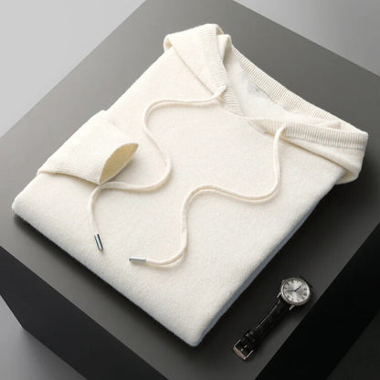 Folded white hoodie on a dark surface with a watch and pen nearby