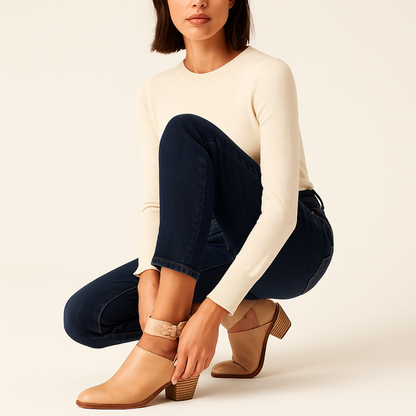 Woman wearing a cream sweater, dark jeans, and tan boots on a beige background