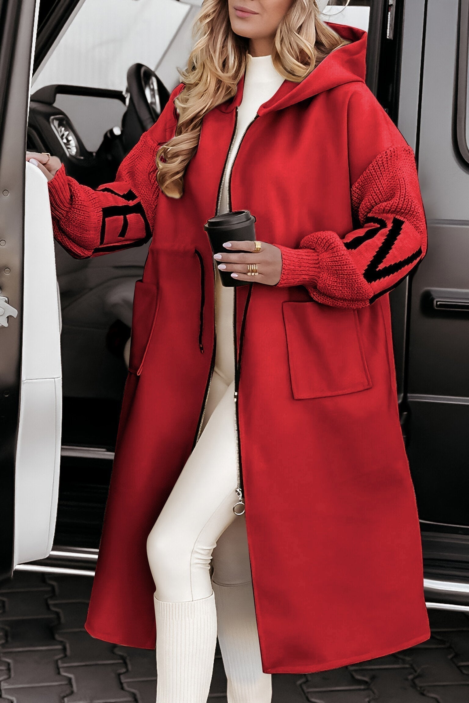 Person wearing a long red coat with black accents, standing next to a vehicle.
