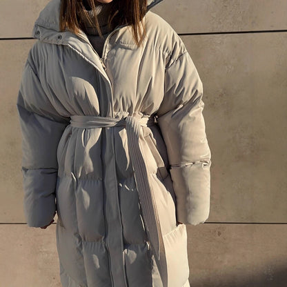 Person wearing a long, light-colored puffer coat against a neutral background