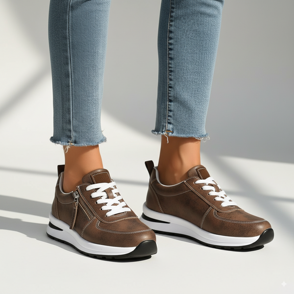 Brown sneakers with white laces worn with light blue jeans on a neutral background